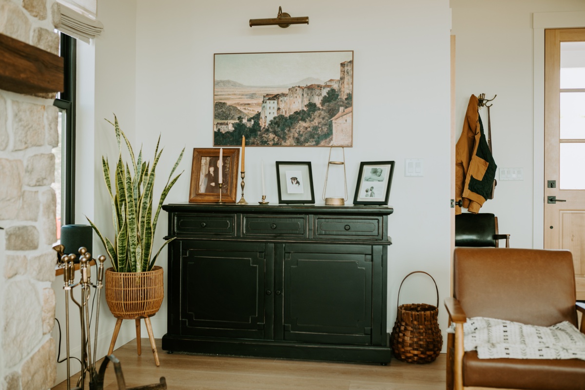 black sideboard with frames and a raised basket potted snake plant