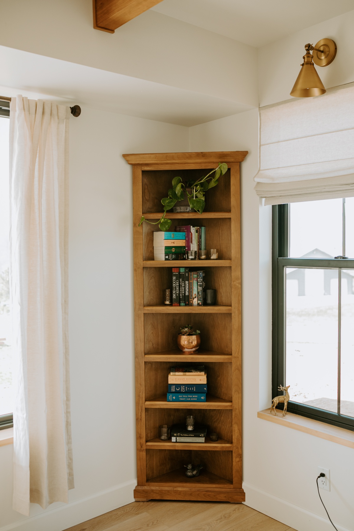 tall corner bookshelf with layered books candles and plants